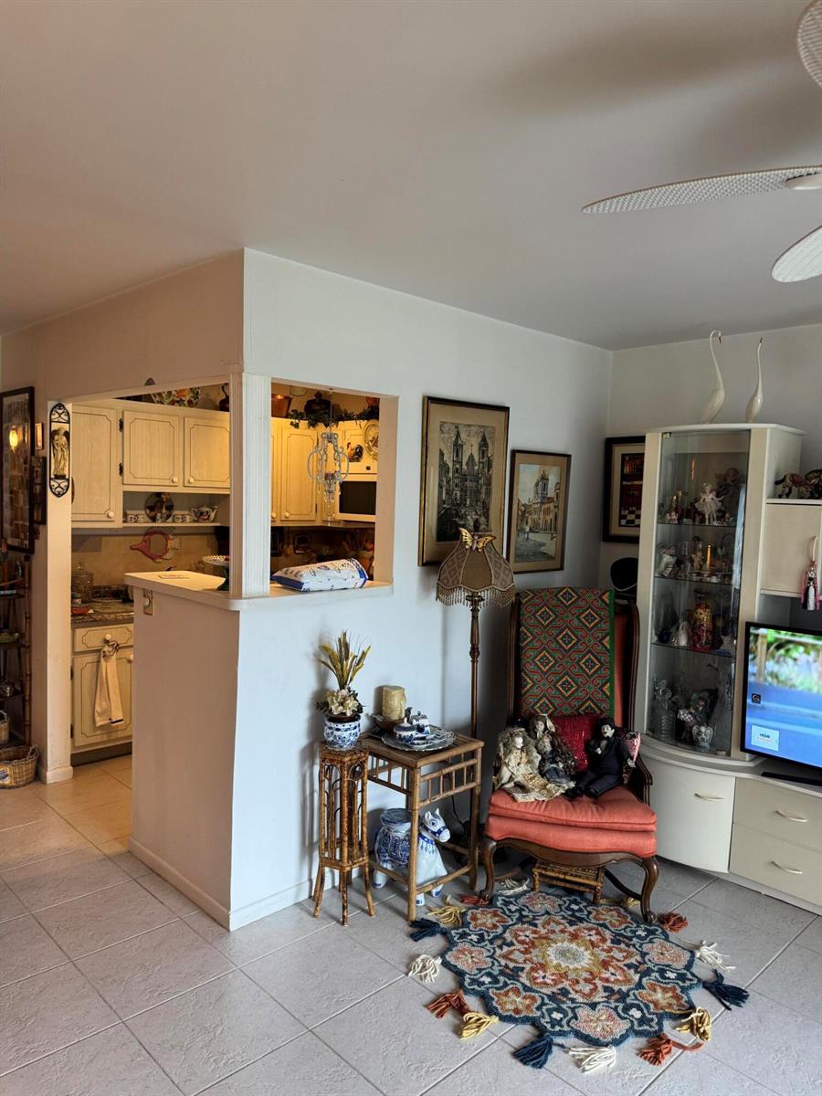 A living room with tile floors, a pass-through kitchen window, and a display cabinet — 90 South Boulevard # 1c, Boynton Beach FL 33435, BOYNTON BEACH, FL