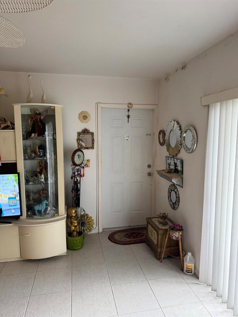 An entryway features white tile flooring, a white front door, and various wall-mounted decorative items — 90 South Boulevard # 1c, Boynton Beach FL 33435, BOYNTON BEACH, FL