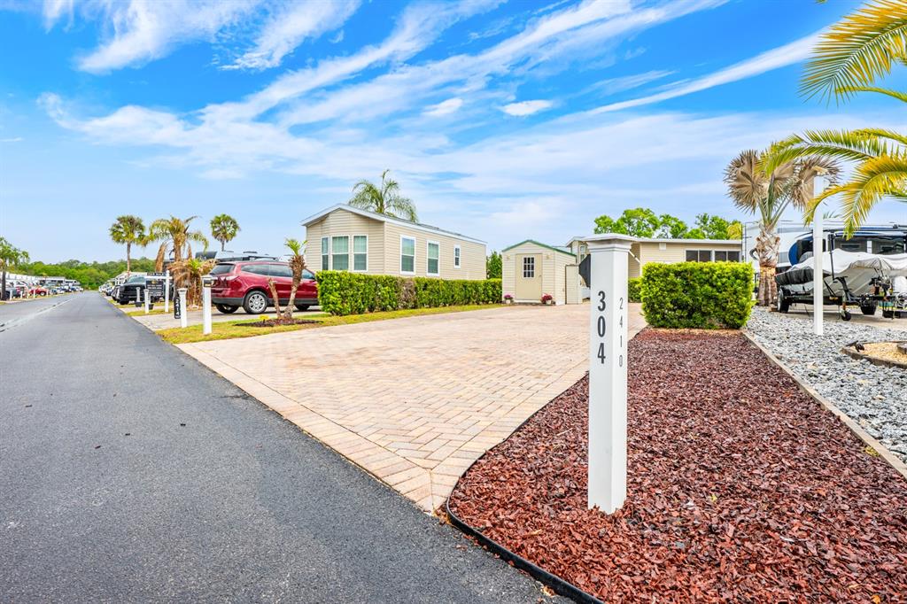 A paved driveway leads to a manufactured home with a small shed and palm trees — 2410 LIMEWOOD AVENUE UNIT 304, CLERMONT, FL