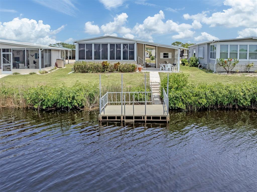 A waterfront mobile home features a private dock, a screened porch, and a grassy yard — 132 MARTINIQUE ROAD, NORTH PORT, FL