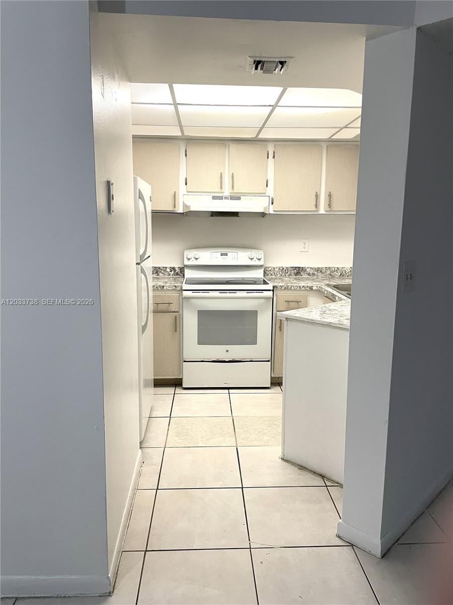 A galley-style kitchen features white appliances, light wood cabinets, and a tiled floor — 8255 SW 152nd Ave # 405, Miami FL 33193, MIAMI, FL