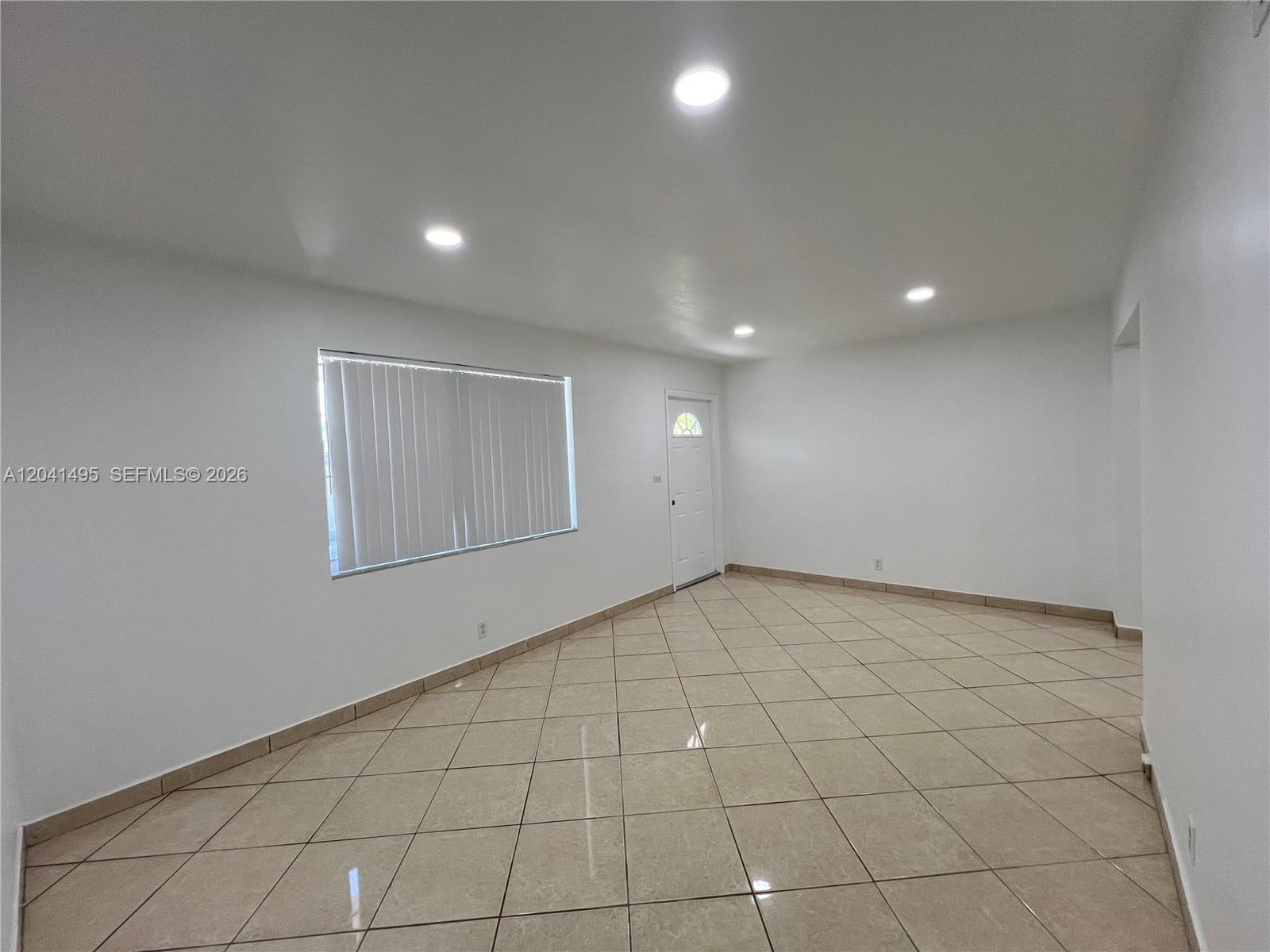 An empty room features white walls, recessed lighting, and light-colored diagonal floor tiles — MIAMI, FL