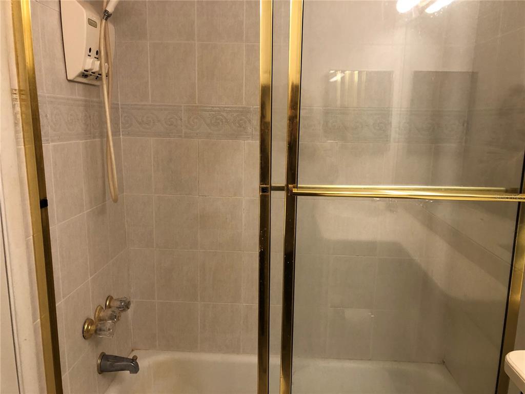 A shower and bathtub combination features light-colored wall tiles and a gold-framed glass door — 6344 NEWTOWN CIRCLE UNIT 44A1, TAMPA, FL