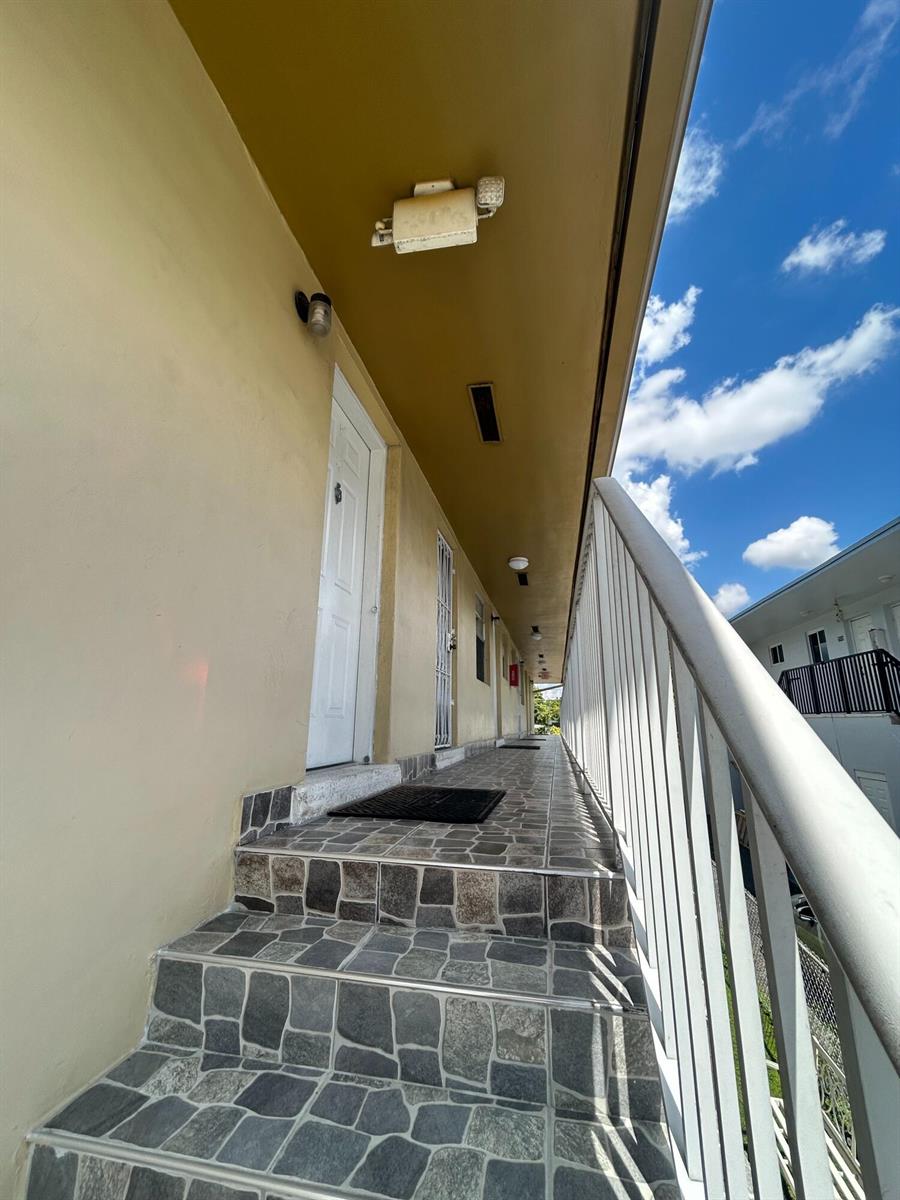 An exterior walkway with stone-tiled stairs and a white metal railing under a blue sky — 715 W 29th Street, Hialeah FL 33012, HIALEAH, FL