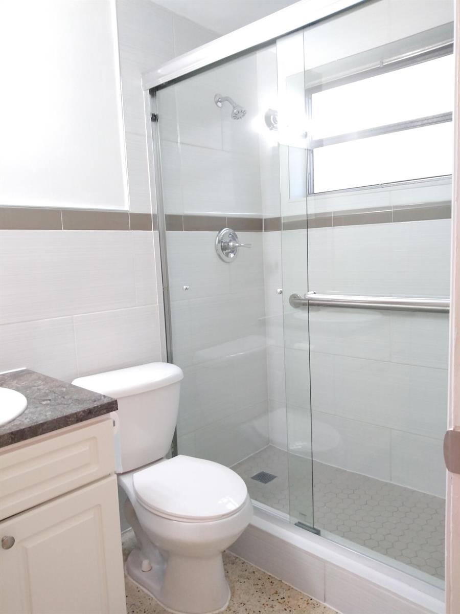 A bathroom features a white toilet, a vanity with a dark countertop, and a glass-enclosed shower — 715 W 29th Street, Hialeah FL 33012, HIALEAH, FL