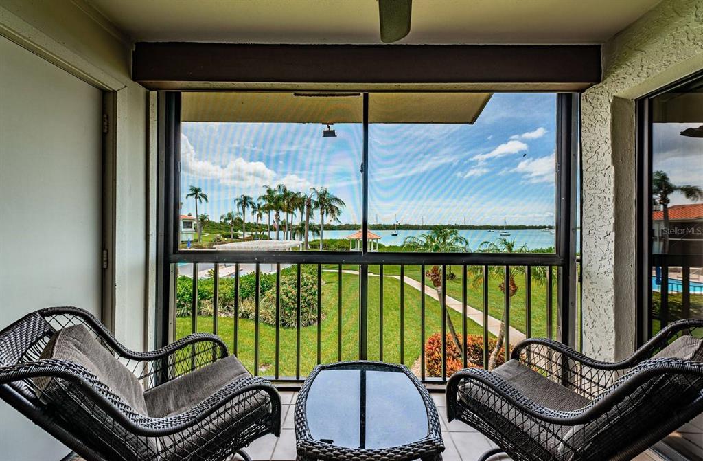 A screened-in balcony features two wicker chairs, a small table, and a waterfront view — 6295 BAHIA DEL MAR CIRCLE UNIT 204, ST PETERSBURG, FL