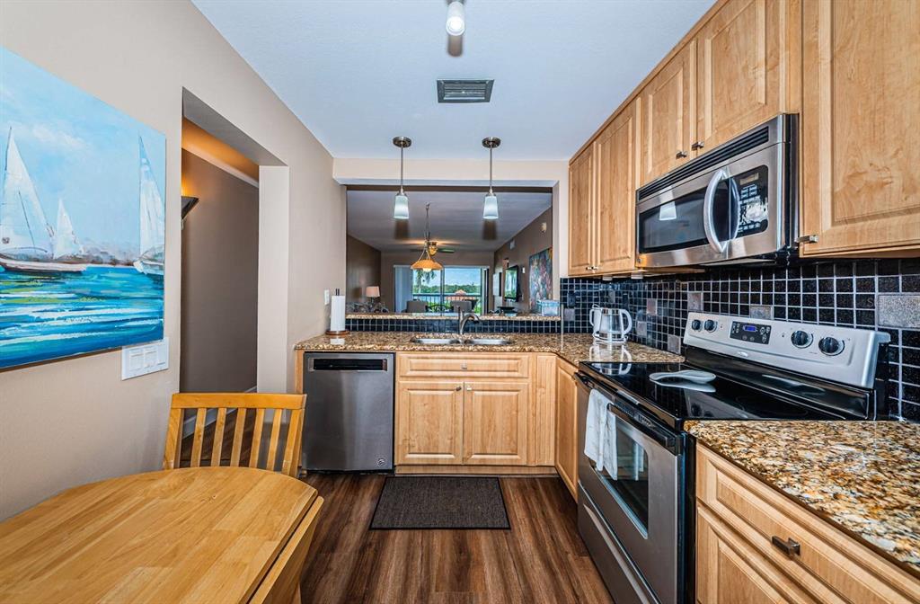 A kitchen features light wood cabinets, stainless steel appliances, granite countertops, and a black backsplash — 6295 BAHIA DEL MAR CIRCLE UNIT 204, ST PETERSBURG, FL