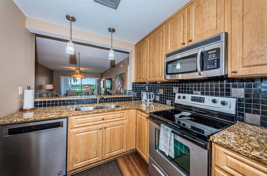 A kitchen with wood cabinets, granite countertops, stainless steel appliances, and a black tile backsplash — 6295 BAHIA DEL MAR CIRCLE UNIT 204, ST PETERSBURG, FL