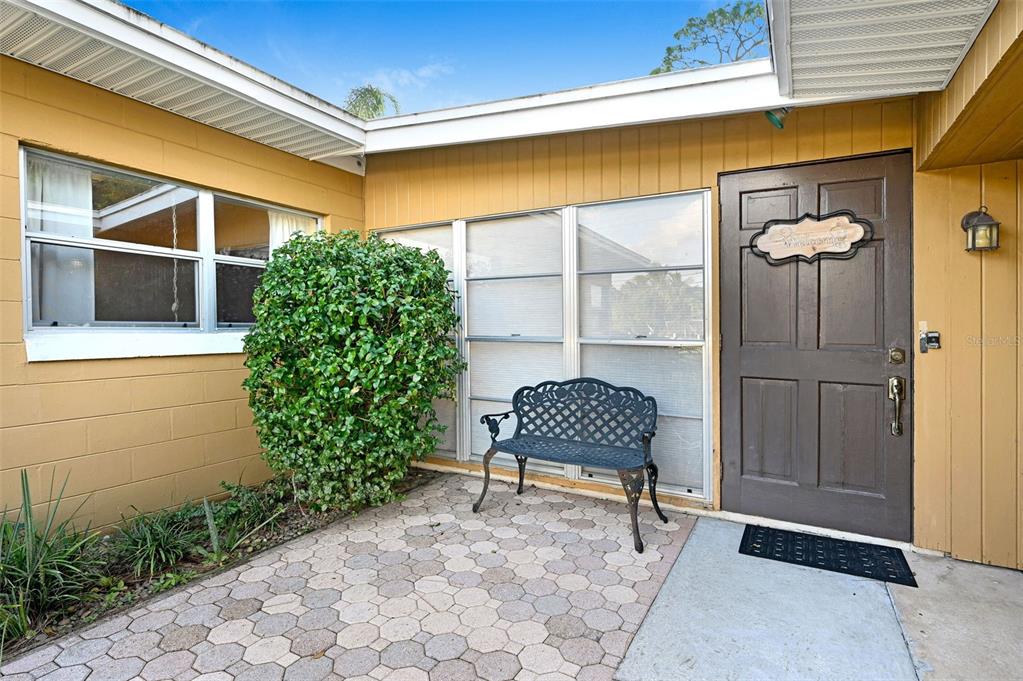 A paved entryway features a dark brown door, a metal bench, and a large shrub — 2885 S TROPICAL TRAIL, MERRITT ISLAND, FL