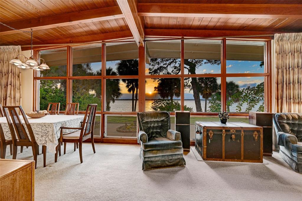 A dining and living area with wood-beamed ceilings, carpeted floors, and large windows overlooking water — 2885 S TROPICAL TRAIL, MERRITT ISLAND, FL
