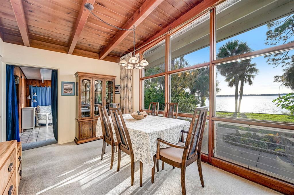 A dining room with a wood-beamed ceiling, carpeted floor, and large windows overlooking a lake — 2885 S TROPICAL TRAIL, MERRITT ISLAND, FL
