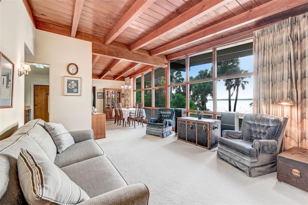 A living room with a wood-beamed ceiling, large windows overlooking a lake, and carpeted floors — 2885 S TROPICAL TRAIL, MERRITT ISLAND, FL