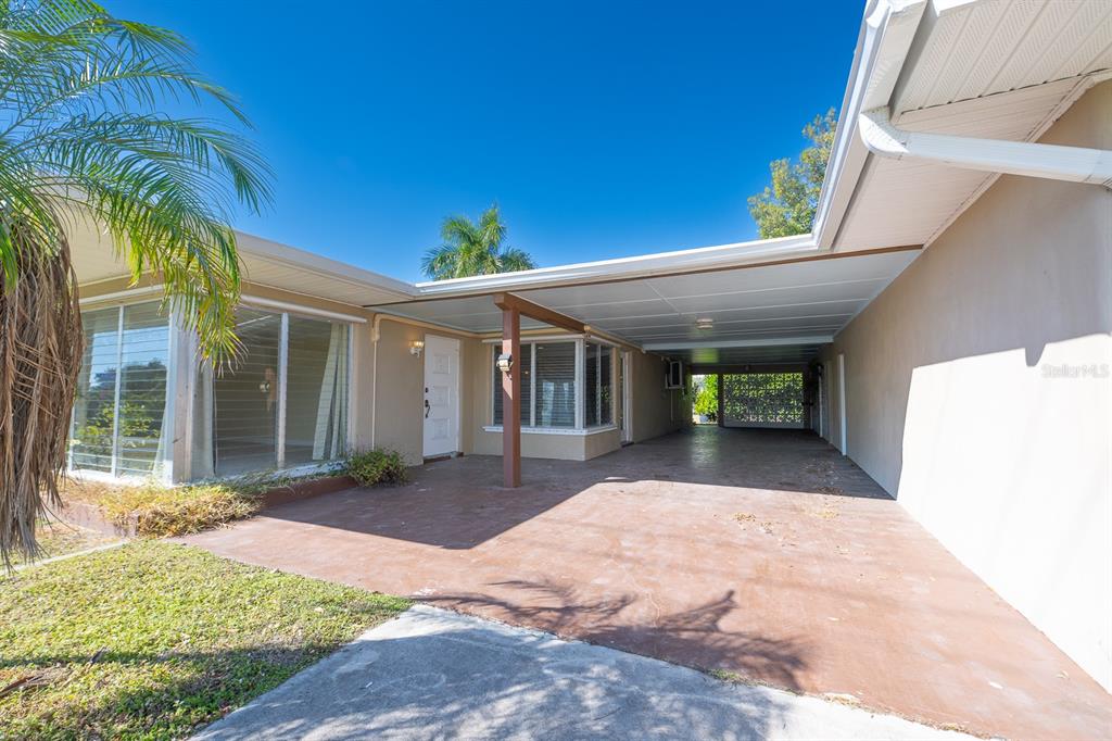 A single-story house exterior features a covered carport, a concrete driveway, and large glass windows — 410 W CHARLOTTE AVENUE, PUNTA GORDA, FL