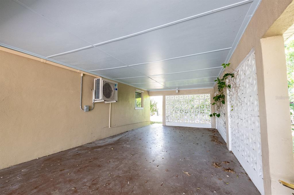 A covered carport features a concrete floor, tan walls, and decorative white breeze block screens — 410 W CHARLOTTE AVENUE, PUNTA GORDA, FL