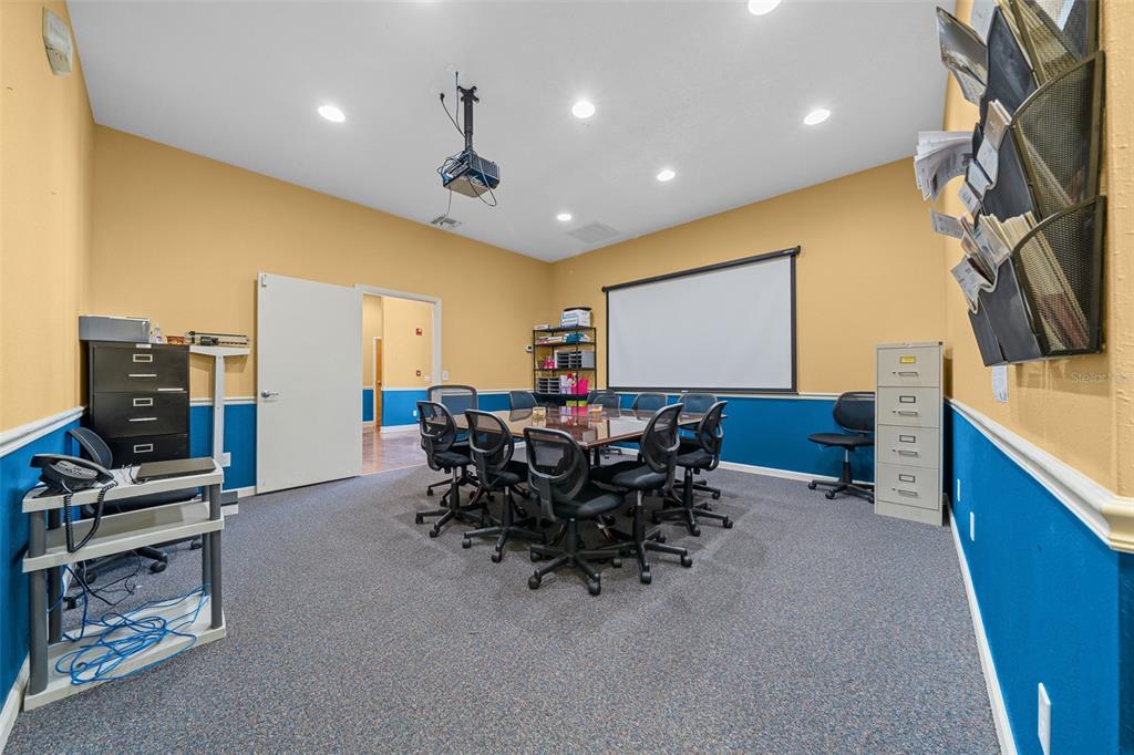 A conference room features a central table, rolling chairs, a projector screen, and blue wainscoting — 5925 SE ABSHIER BOULEVARD, BELLEVIEW, FL