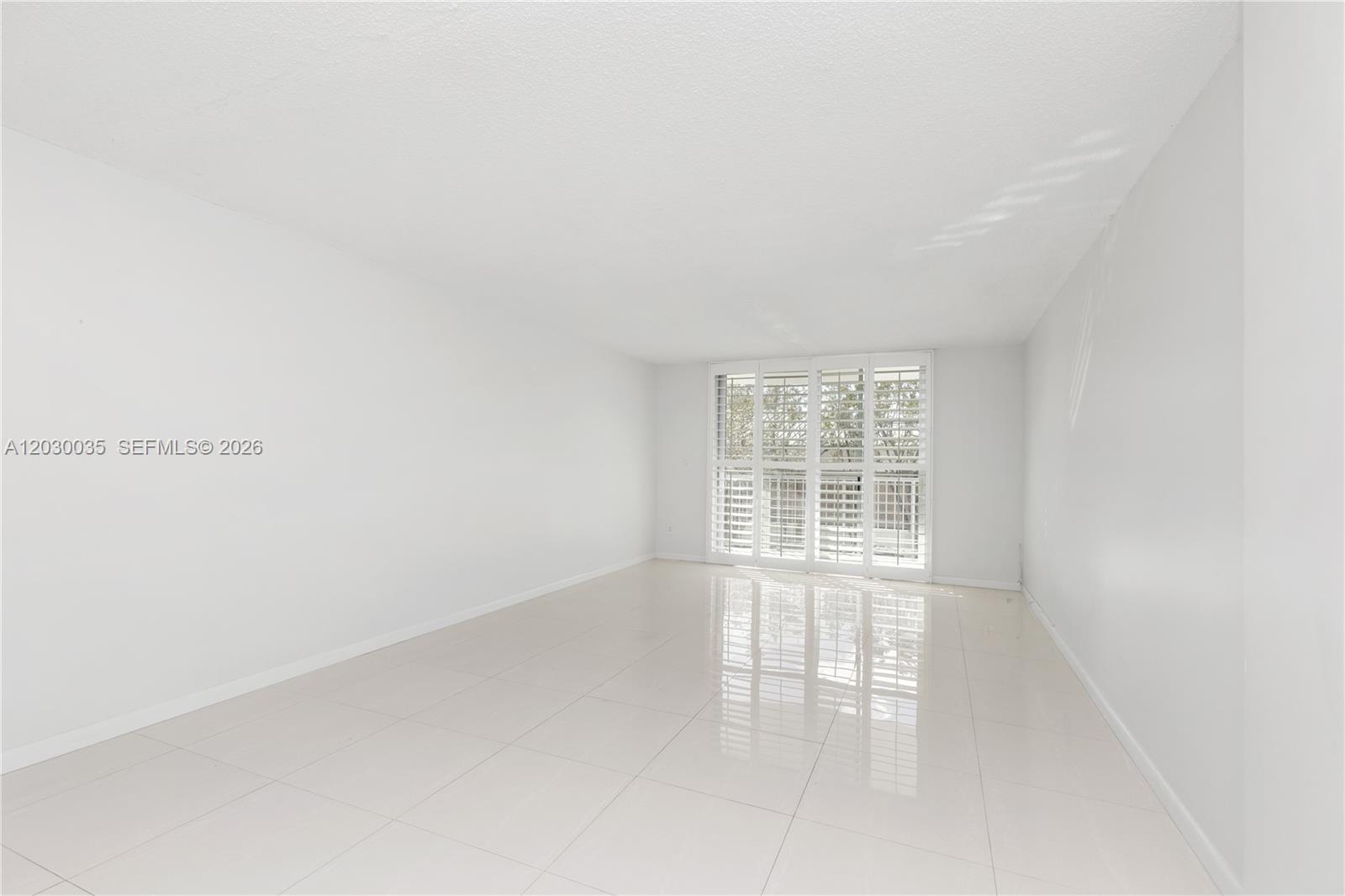 A bright, empty room features white walls, glossy tile flooring, and floor-to-ceiling plantation shutters — 210 Sea View Dr # 207, Key Biscayne FL 33149, KEY BISCAYNE, FL