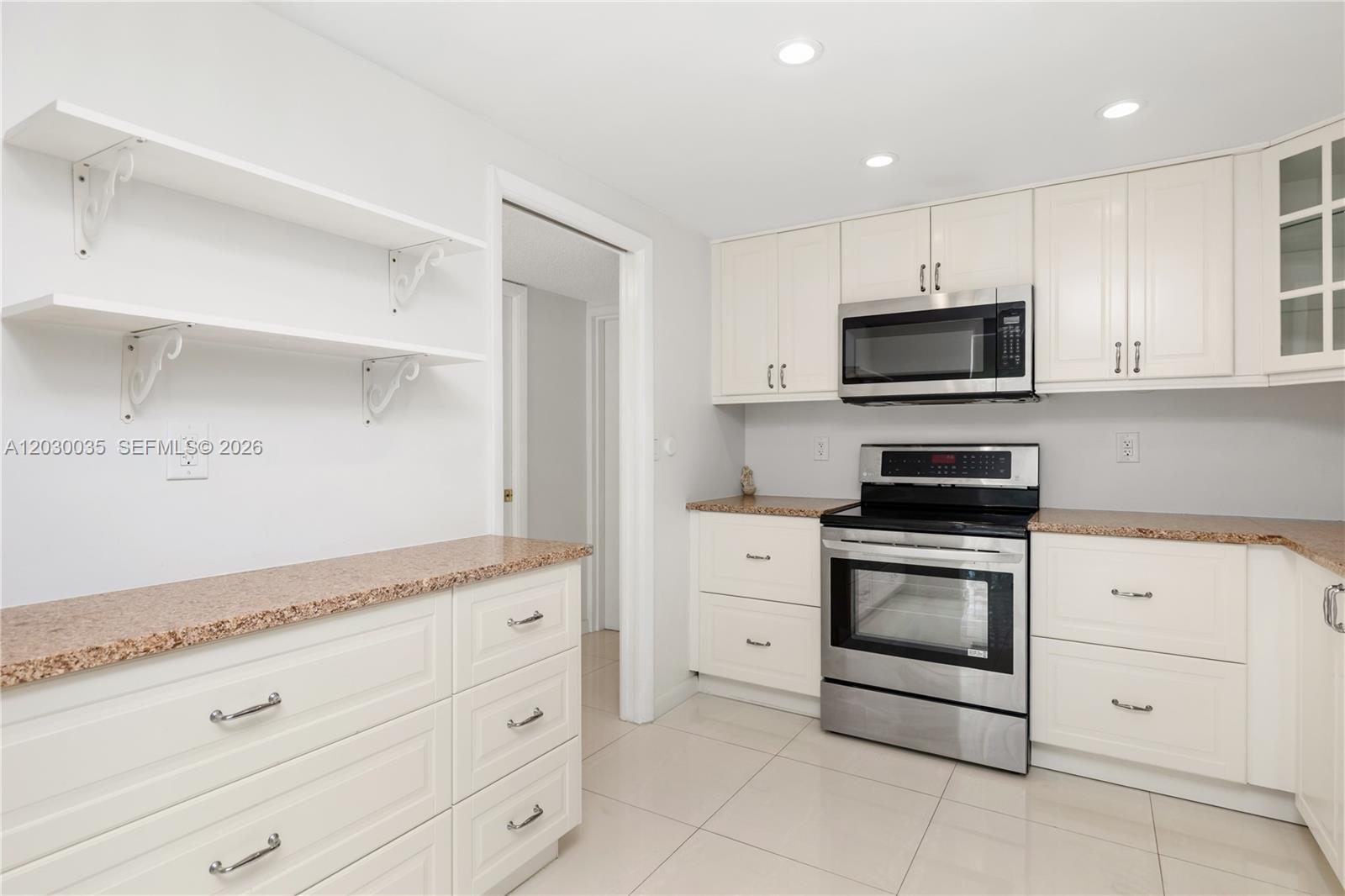 A kitchen features white cabinets, stainless steel appliances, granite countertops, and open wall shelving — 210 Sea View Dr # 207, Key Biscayne FL 33149, KEY BISCAYNE, FL