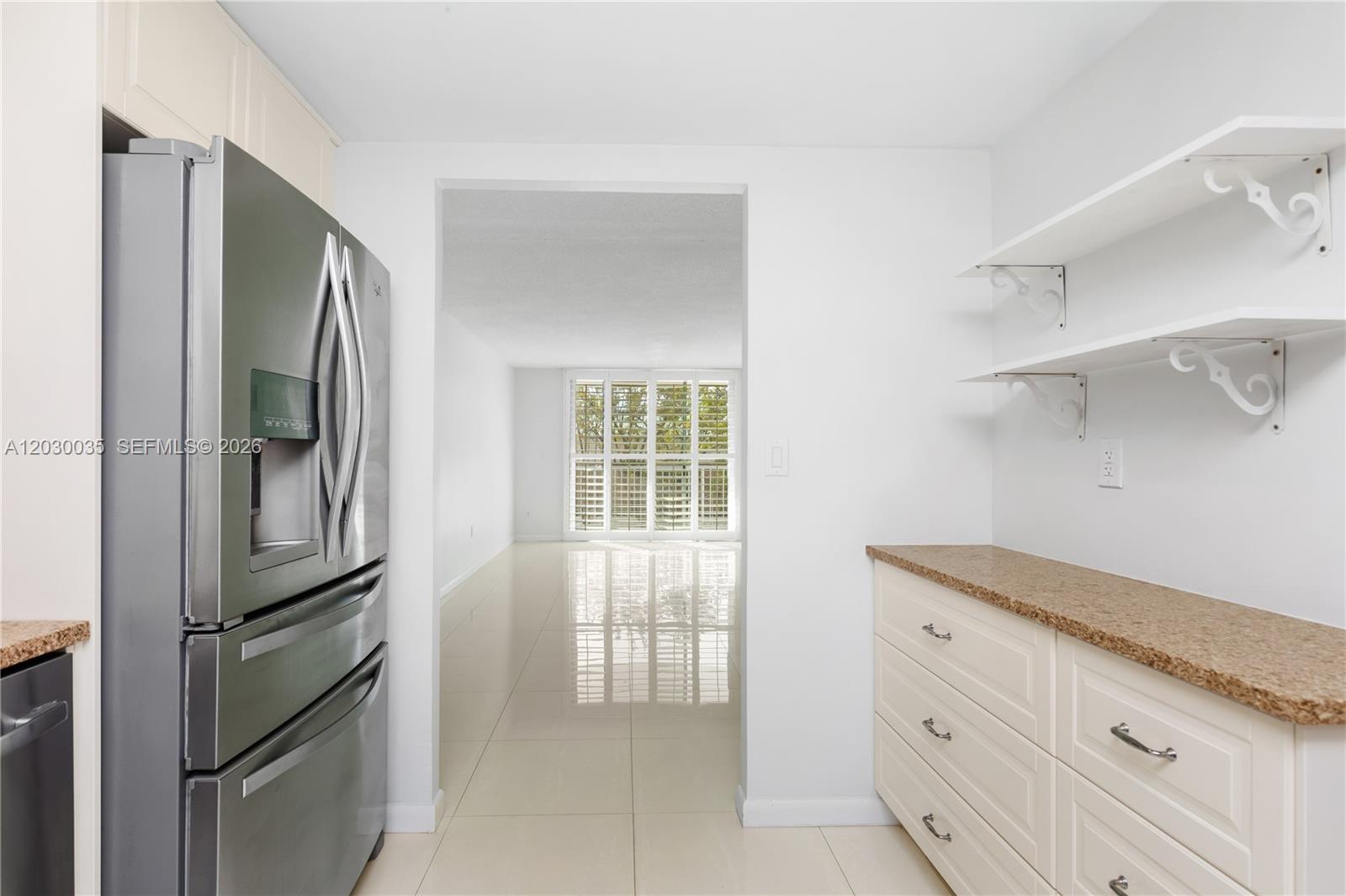A kitchen features a stainless steel refrigerator, white cabinetry, granite countertops, and open shelving — 210 Sea View Dr # 207, Key Biscayne FL 33149, KEY BISCAYNE, FL
