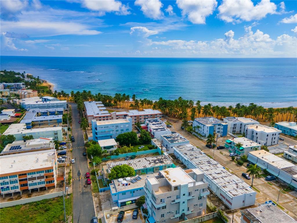 An aerial view shows multiple apartment buildings situated along a sandy beach and ocean — 707 OCEAN DRIVE UNIT A-4, LUQUILLO, PR