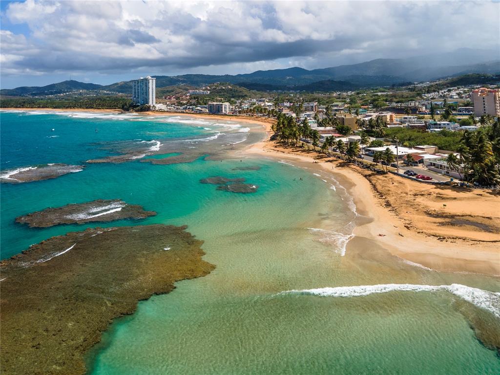 An aerial view of a sandy beach with turquoise water, coral reefs, and coastal buildings — 707 OCEAN DRIVE UNIT A-4, LUQUILLO, PR
