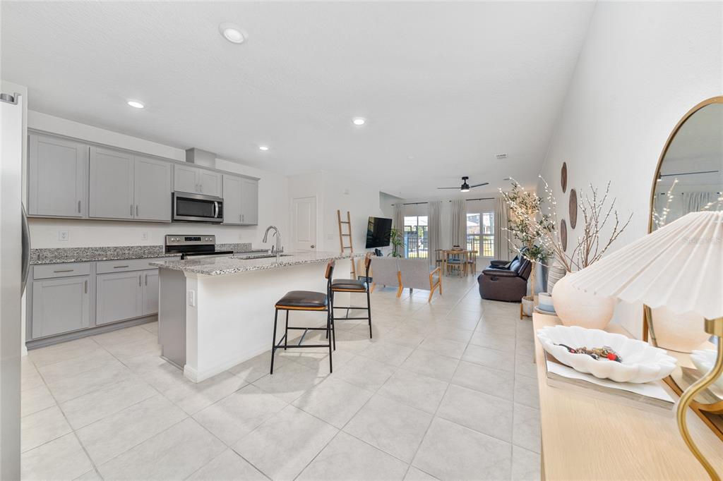 An open-concept kitchen with gray cabinets and granite countertops flows into a living area — 1349 MIRABELLA CIR, DAVENPORT, FL