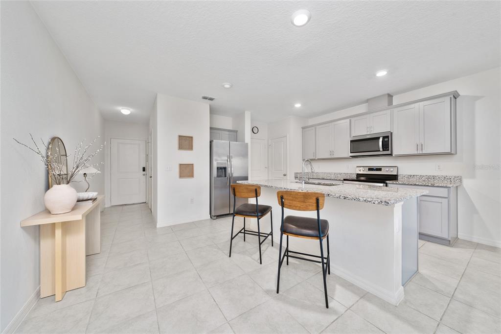 A kitchen features gray cabinets, granite countertops, a stainless steel refrigerator, and two bar stools — 1349 MIRABELLA CIR, DAVENPORT, FL