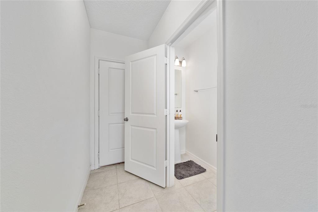 A hallway leads to a bathroom with a pedestal sink and a closed door — 1349 MIRABELLA CIR, DAVENPORT, FL