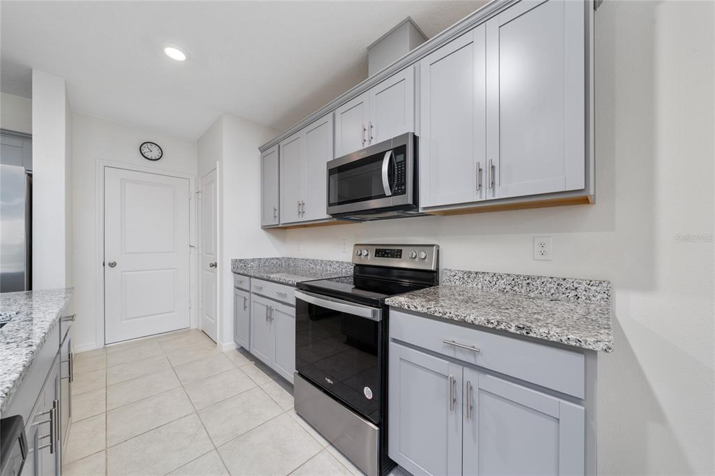 A kitchen features light gray cabinets, granite countertops, and stainless steel appliances — 1349 MIRABELLA CIR, DAVENPORT, FL