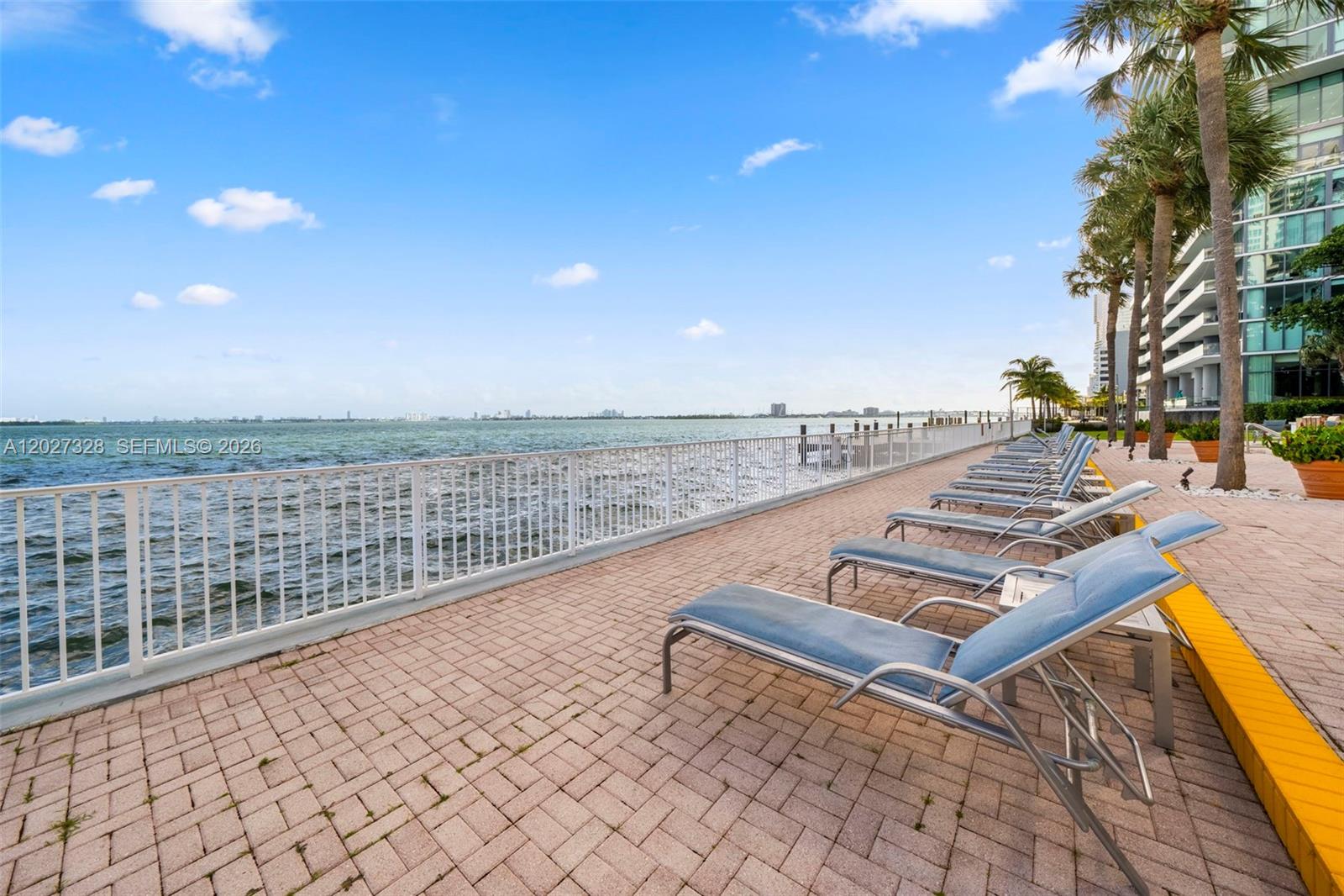 A paved waterfront patio features a row of lounge chairs beside a white metal railing — 3301 NE 5th Ave # 1015, Miami FL 33137, MIAMI, FL