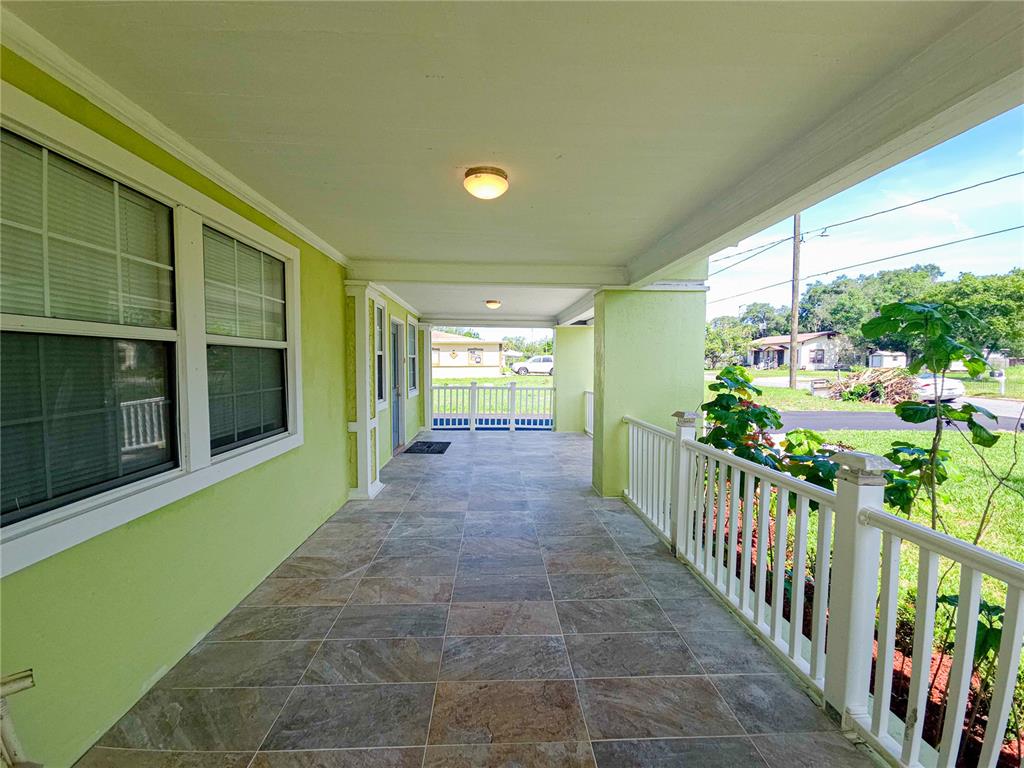 A covered front porch with tiled flooring and white railings overlooks a residential street — 17 WILKES STREET, AVON PARK, FL