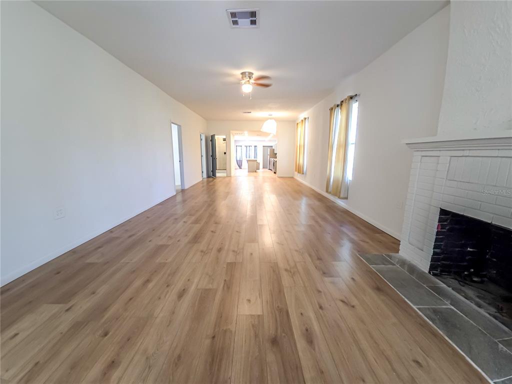 A long living room features light wood-look flooring, white walls, and a white brick fireplace — 17 WILKES STREET, AVON PARK, FL