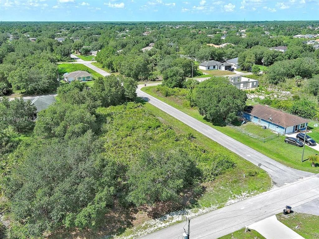 An aerial view shows a vacant, wooded lot situated between residential houses and paved roads — 2517 67TH STREET W, LEHIGH ACRES, FL