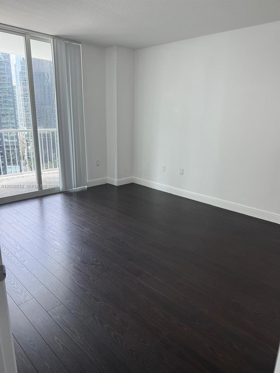 An empty room features dark wood flooring, white walls, and a sliding glass balcony door — 1250 S Miami Ave # 1412, Miami FL 33130, MIAMI, FL
