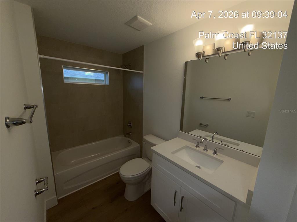 A bathroom features a white vanity, a toilet, and a bathtub with tiled walls — 85 LARAMIE DRIVE, PALM COAST, FL