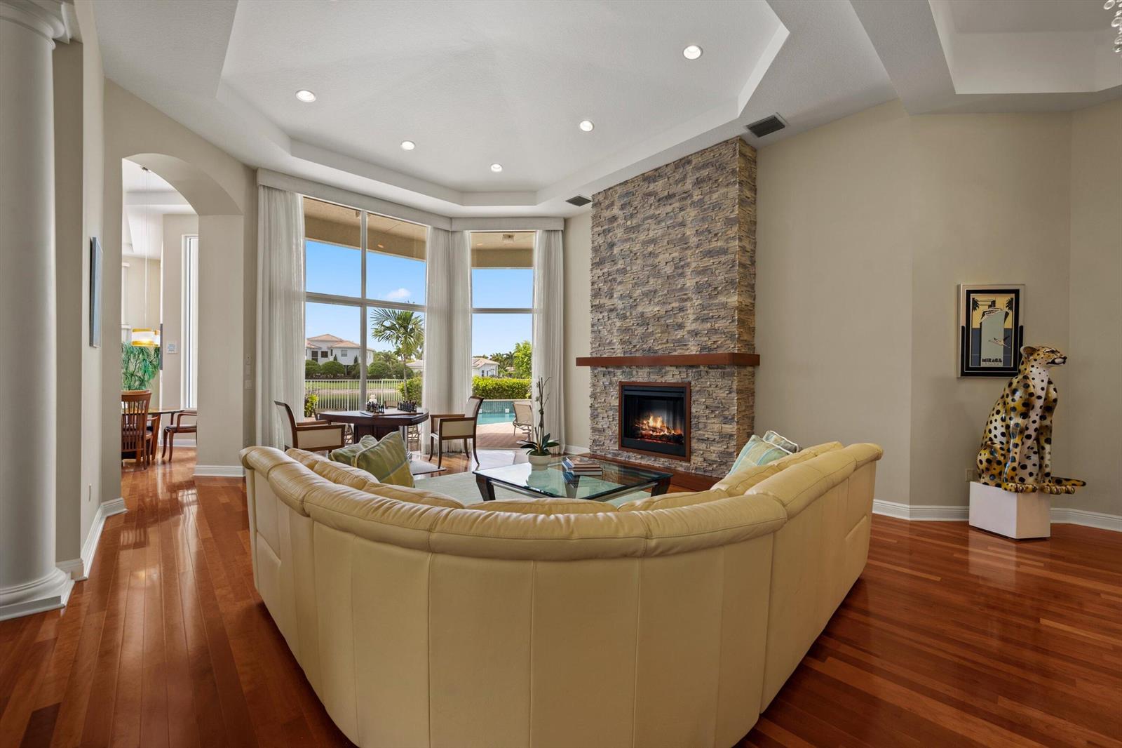 A living room features a stone fireplace, curved leather sofa, and large windows overlooking a pool — 2792 Pillsbury Way, Wellington FL 33414, WELLINGTON, FL