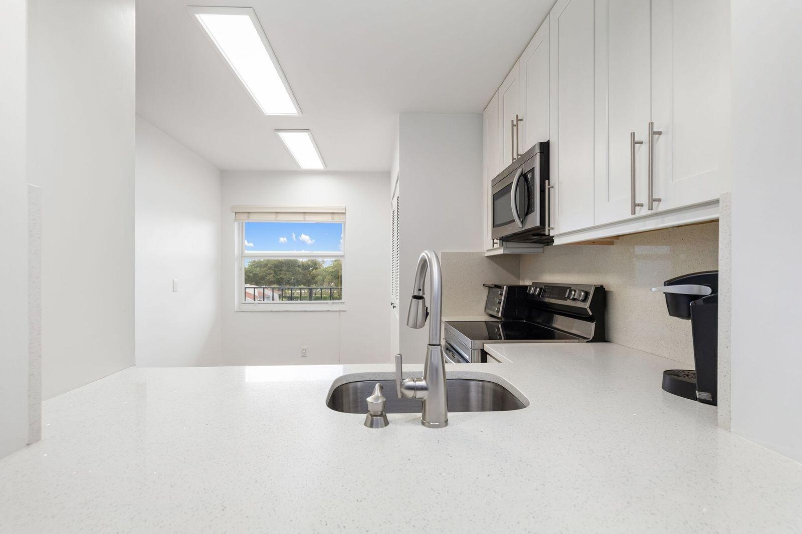 A kitchen features white cabinets, a stainless steel sink, and a window overlooking the outdoors — 6650 S Oriole Boulevard # 4080, Delray Beach FL 33446, DELRAY BEACH, FL