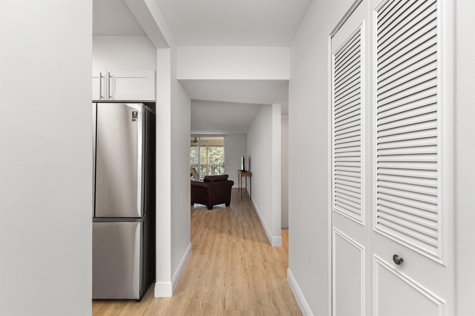 A hallway with light wood flooring leads past a stainless steel refrigerator to a living area — 6650 S Oriole Boulevard # 4080, Delray Beach FL 33446, DELRAY BEACH, FL