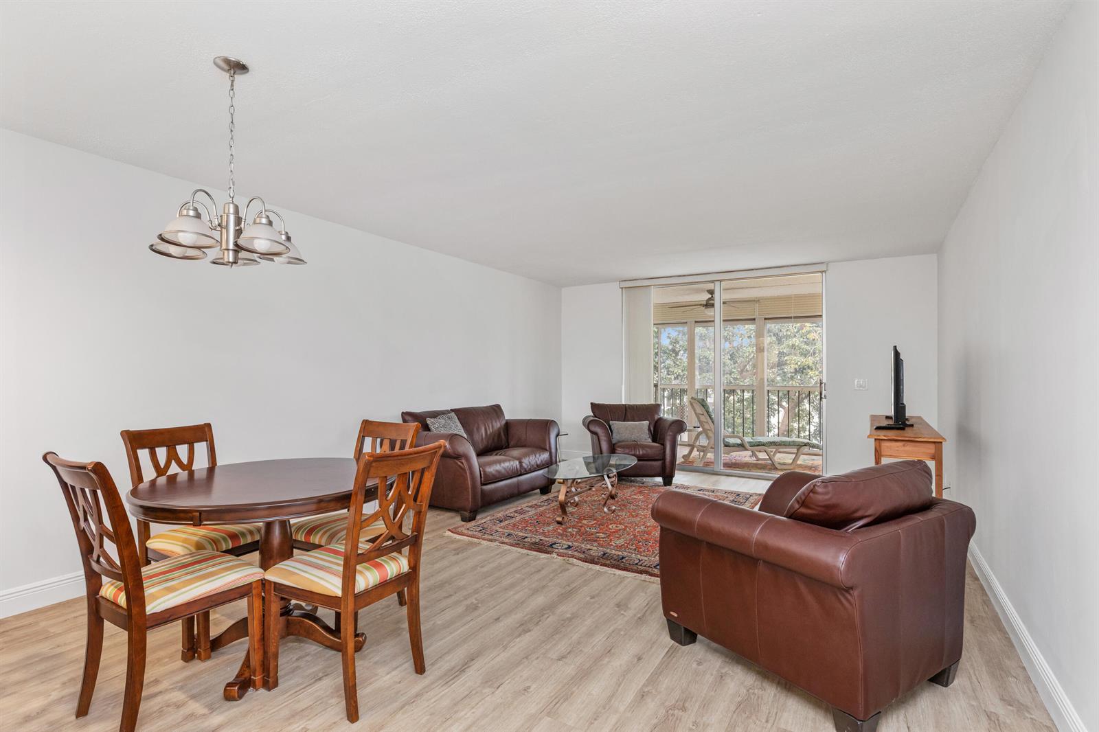 A living and dining area with brown leather furniture, a patterned rug, and a balcony view — 6650 S Oriole Boulevard # 4080, Delray Beach FL 33446, DELRAY BEACH, FL