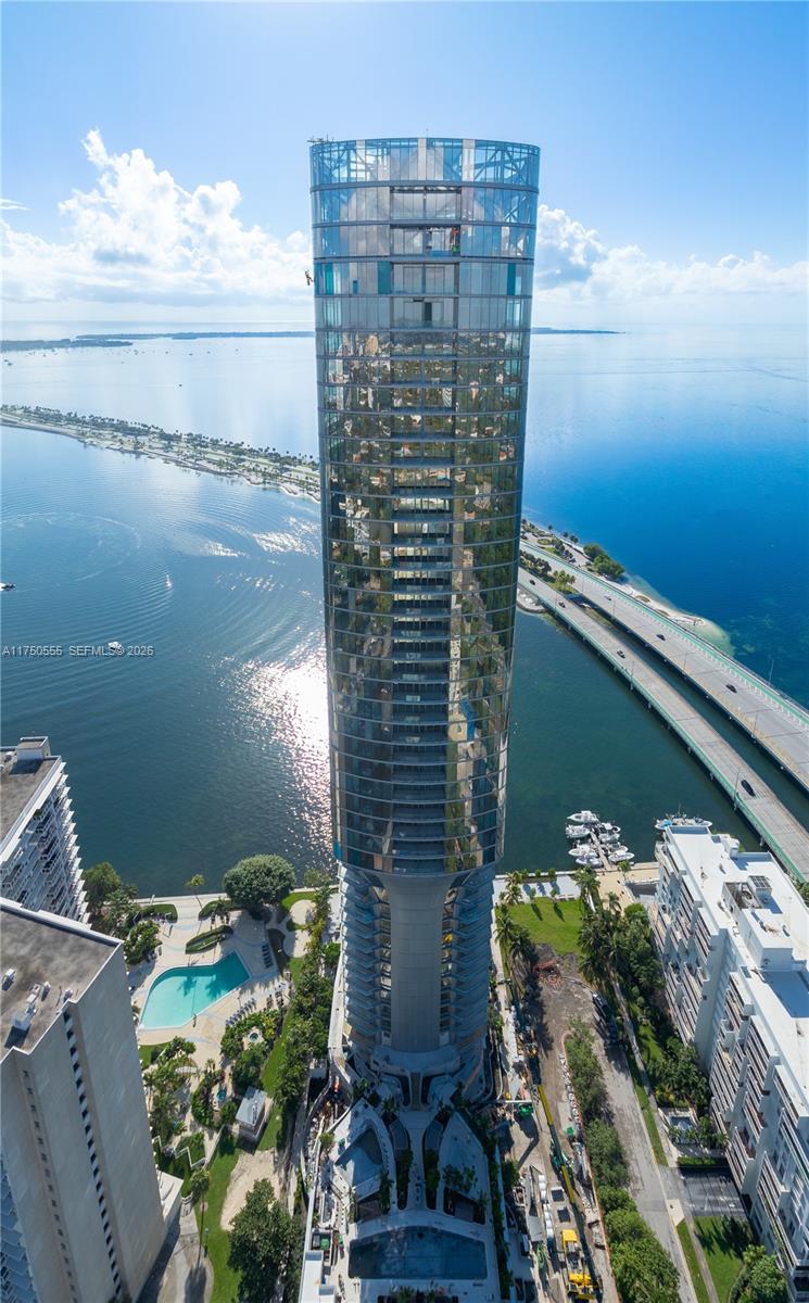 An aerial view shows a tall, cylindrical glass skyscraper surrounded by water and a bridge — 175 SE 25 RD # 3902, Miami FL 33129, MIAMI, FL