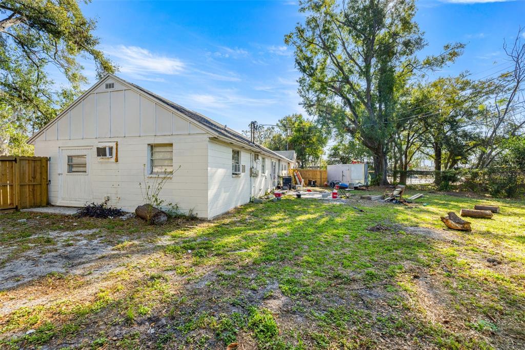 The exterior of a white, single-story house with a large, grassy backyard and mature trees — 1403 COLLEGE PARK LANE, TAMPA, FL