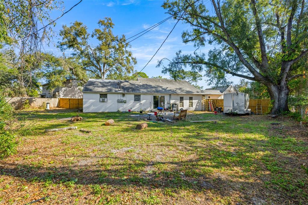 A backyard view of a single-story house with a lawn, trees, and a utility trailer — 1403 COLLEGE PARK LANE, TAMPA, FL