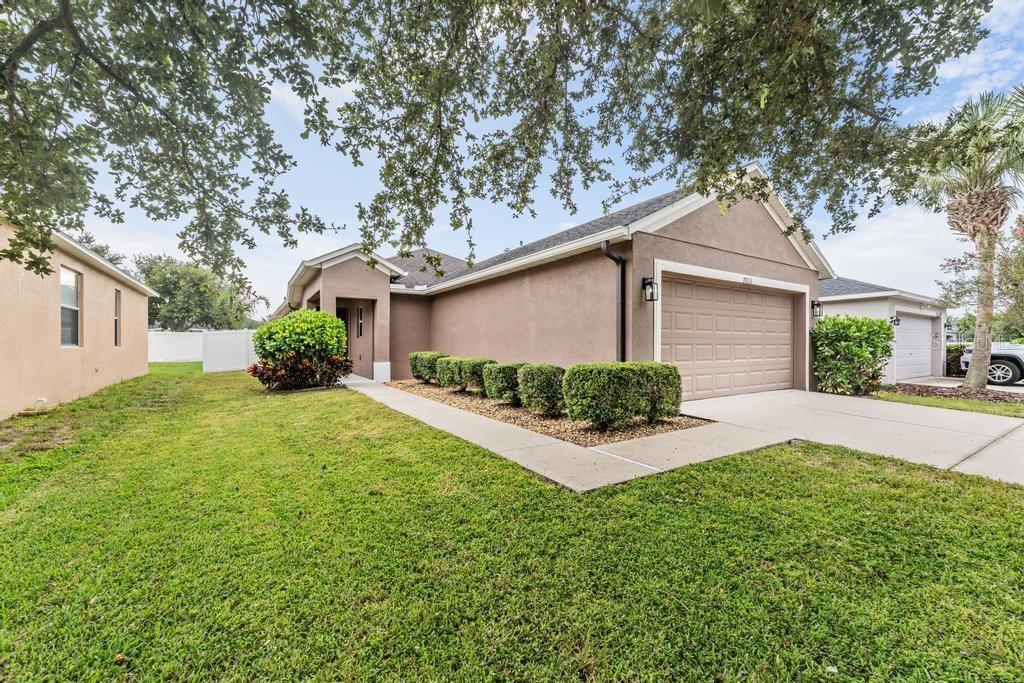 A tan single-story house with a two-car garage, a concrete driveway, and manicured landscaping — 7013 FOREST MERE DRIVE, RIVERVIEW, FL