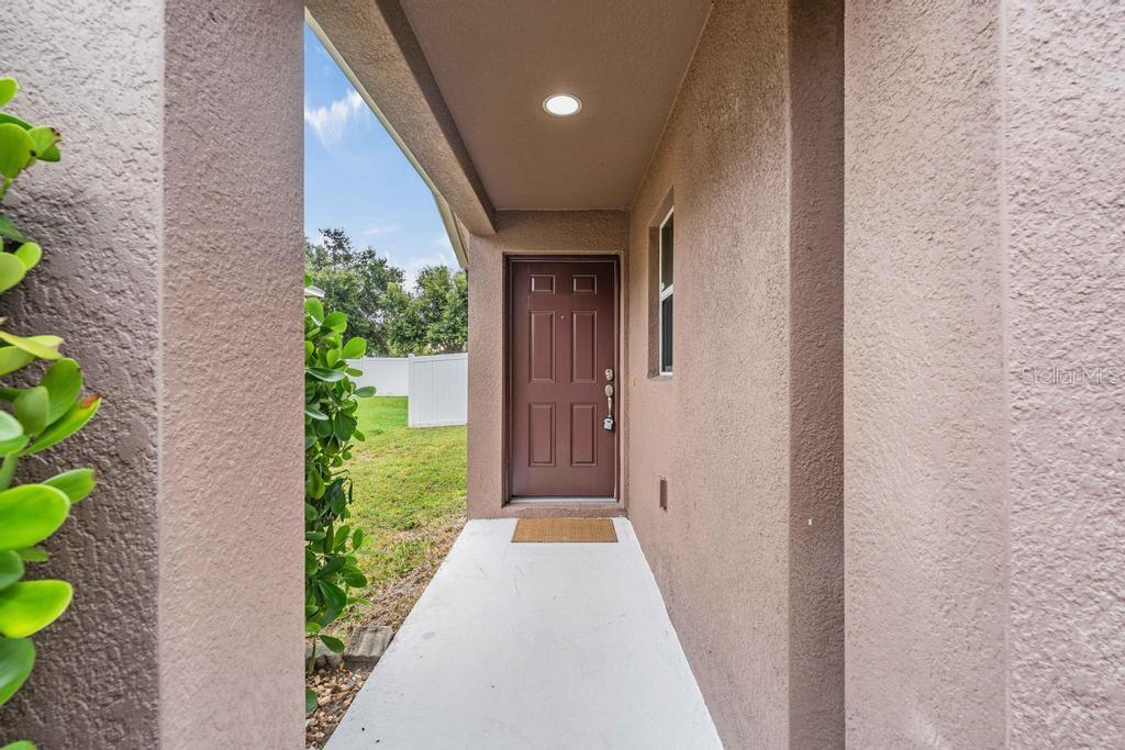 A covered entryway features a brown front door, a concrete floor, and a small doormat — 7013 FOREST MERE DRIVE, RIVERVIEW, FL