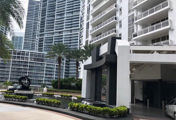A modern high-rise building entrance features a black sculptural fountain and landscaped garden beds — 901 Brickell Key Blvd # 3307, Miami FL 33131, MIAMI, FL