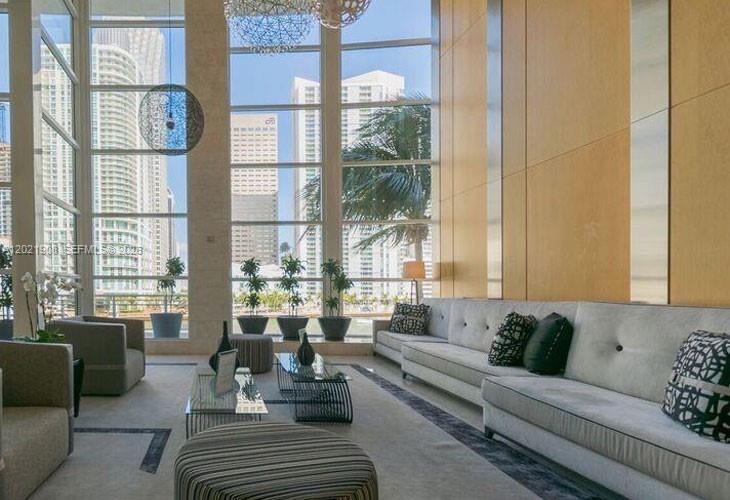 A modern living room features floor-to-ceiling windows, light-colored sofas, and a view of city buildings — 901 Brickell Key Blvd # 3307, Miami FL 33131, MIAMI, FL