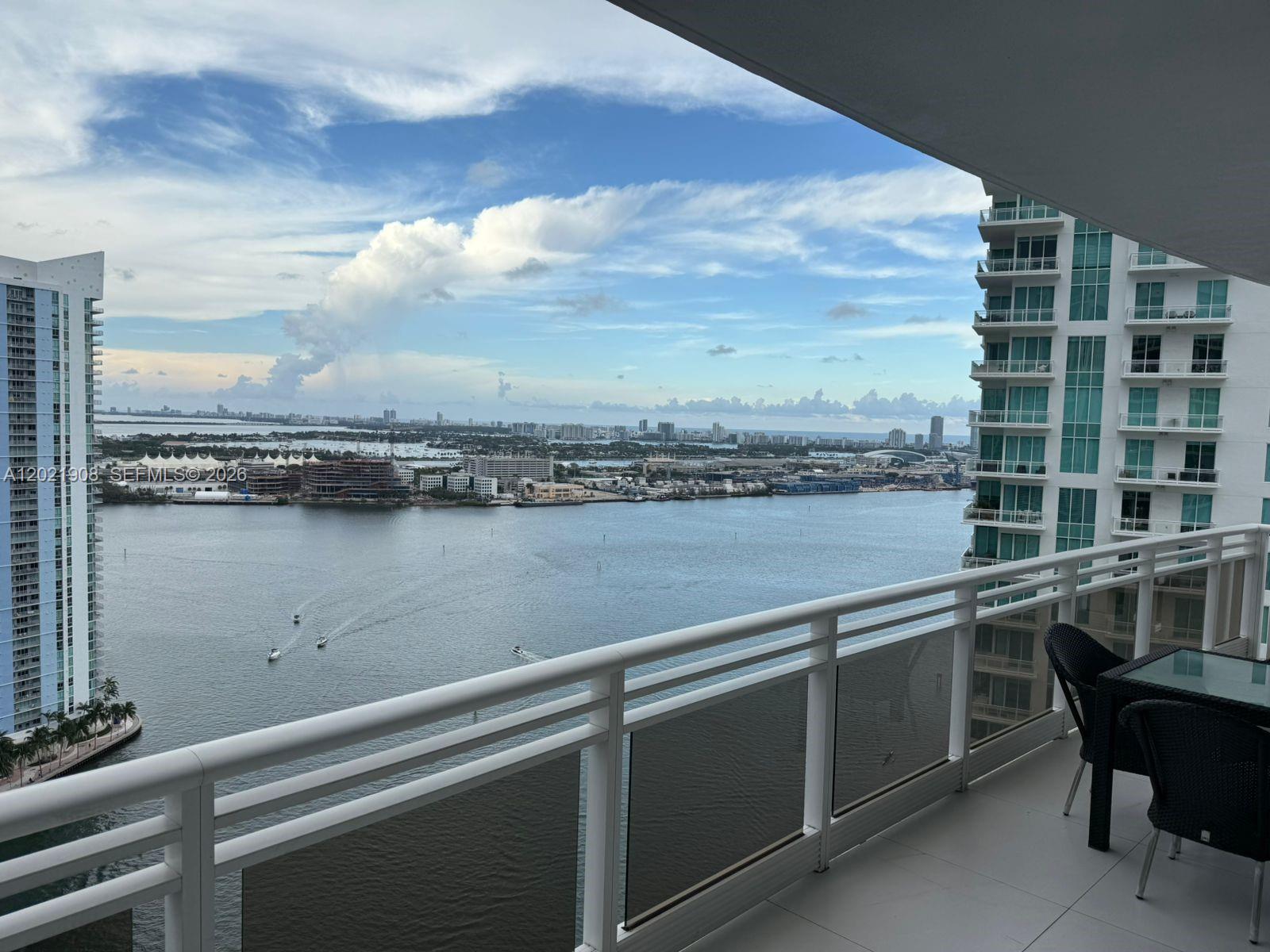 A high-rise balcony overlooks a bay with boats, nearby skyscrapers, and a distant city skyline — 901 Brickell Key Blvd # 3307, Miami FL 33131, MIAMI, FL