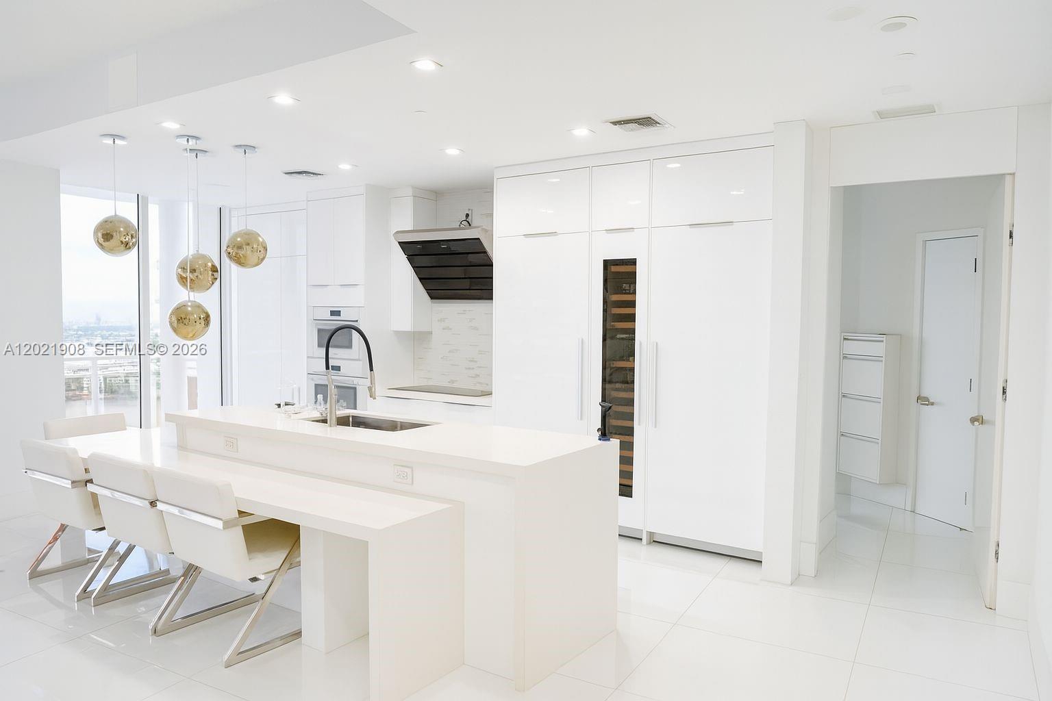 A modern white kitchen features a central island, integrated appliances, and gold pendant lighting — 901 Brickell Key Blvd # 3307, Miami FL 33131, MIAMI, FL