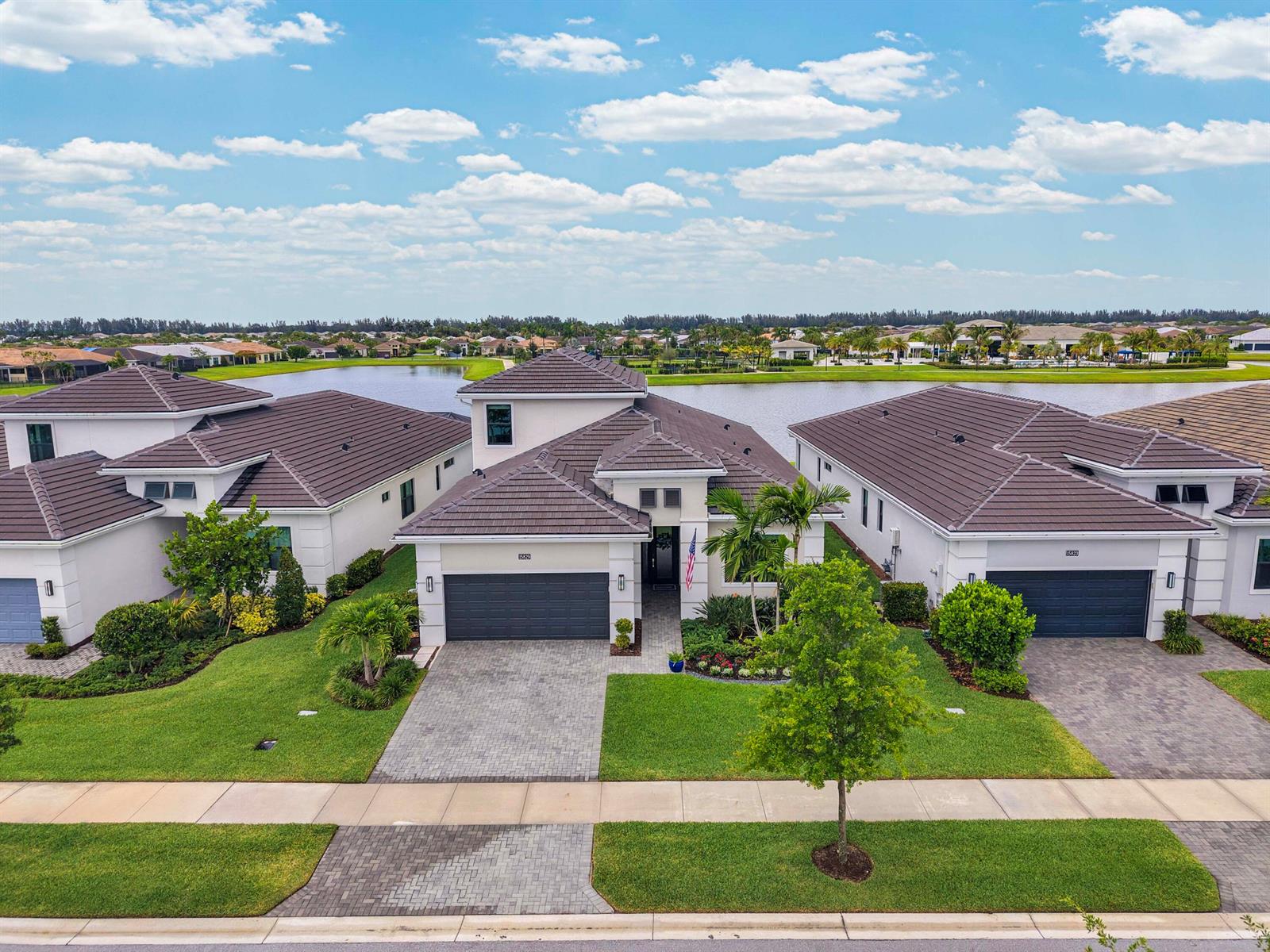 An aerial view shows three modern suburban houses with dark tile roofs facing a lake — 15829 Key Biscayne Lane, Westlake FL 33470, WESTLAKE, FL