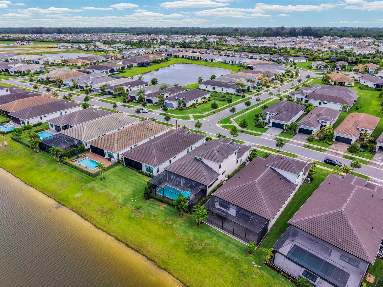 An aerial view shows a suburban neighborhood with houses, swimming pools, and a central pond — 15829 Key Biscayne Lane, Westlake FL 33470, WESTLAKE, FL