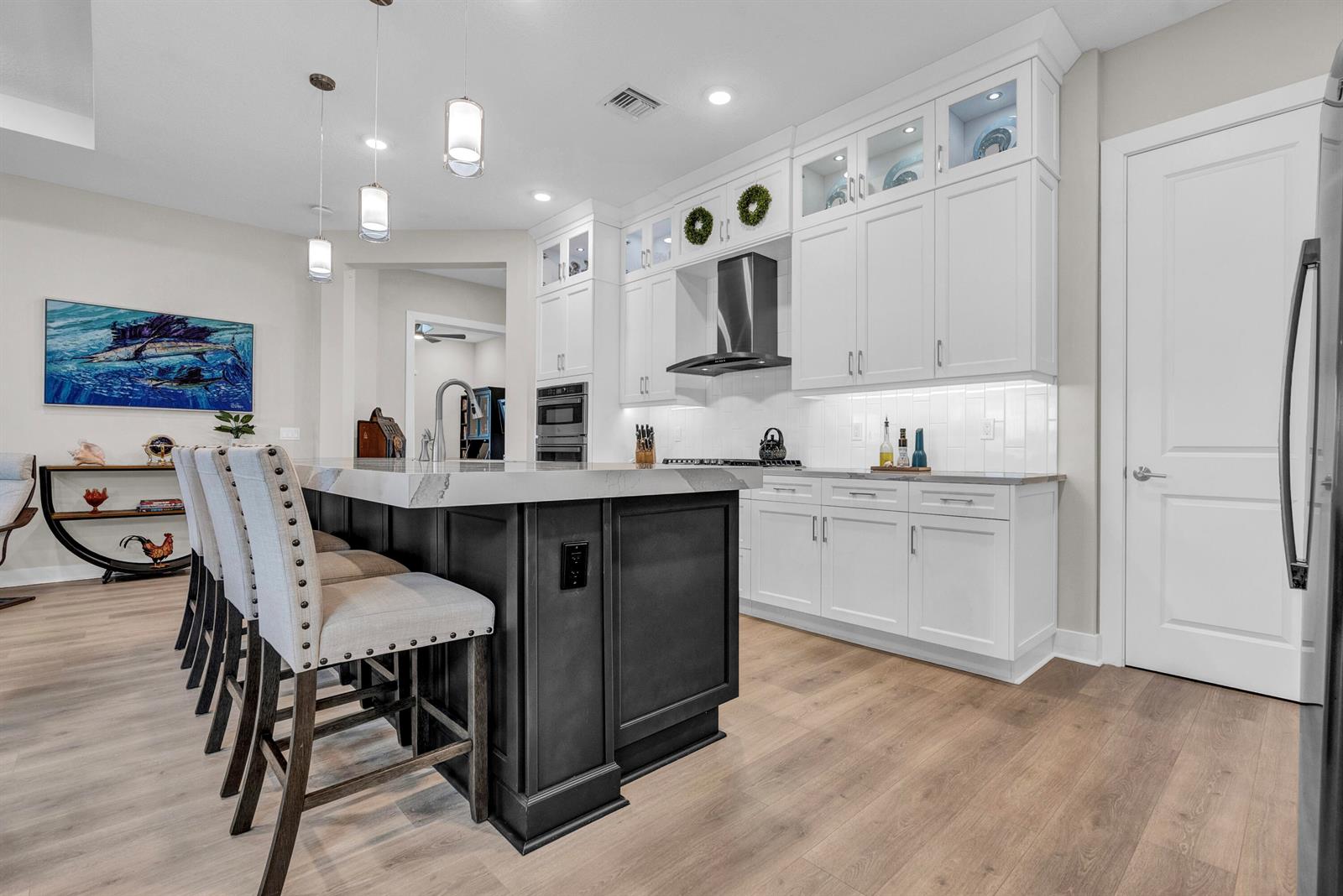 A modern kitchen features a dark island with bar seating, white cabinetry, and wood flooring — 15829 Key Biscayne Lane, Westlake FL 33470, WESTLAKE, FL